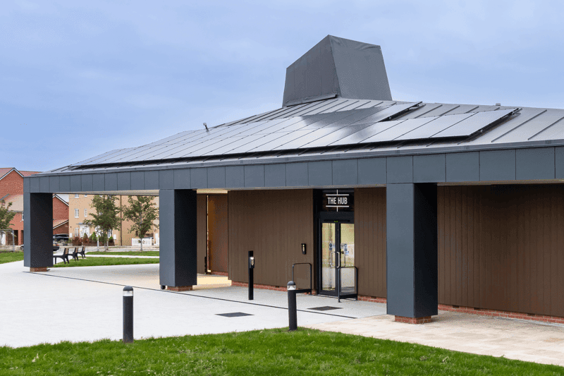 Modern building with a flat roof and solar panels, featuring a glass entrance and landscaped lawn in front.