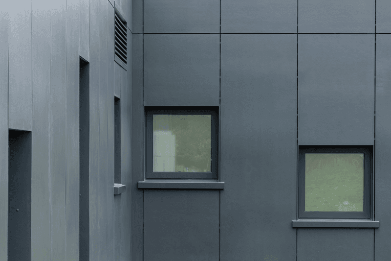 Close-up of a gray building corner with two small windows, featuring a minimalist design and sleek surfaces.